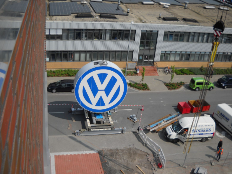 Montage eines großen Volkswagen Logos durch Stahlbau Sanders mit Projektfahrzeug vor VW-Gebäude